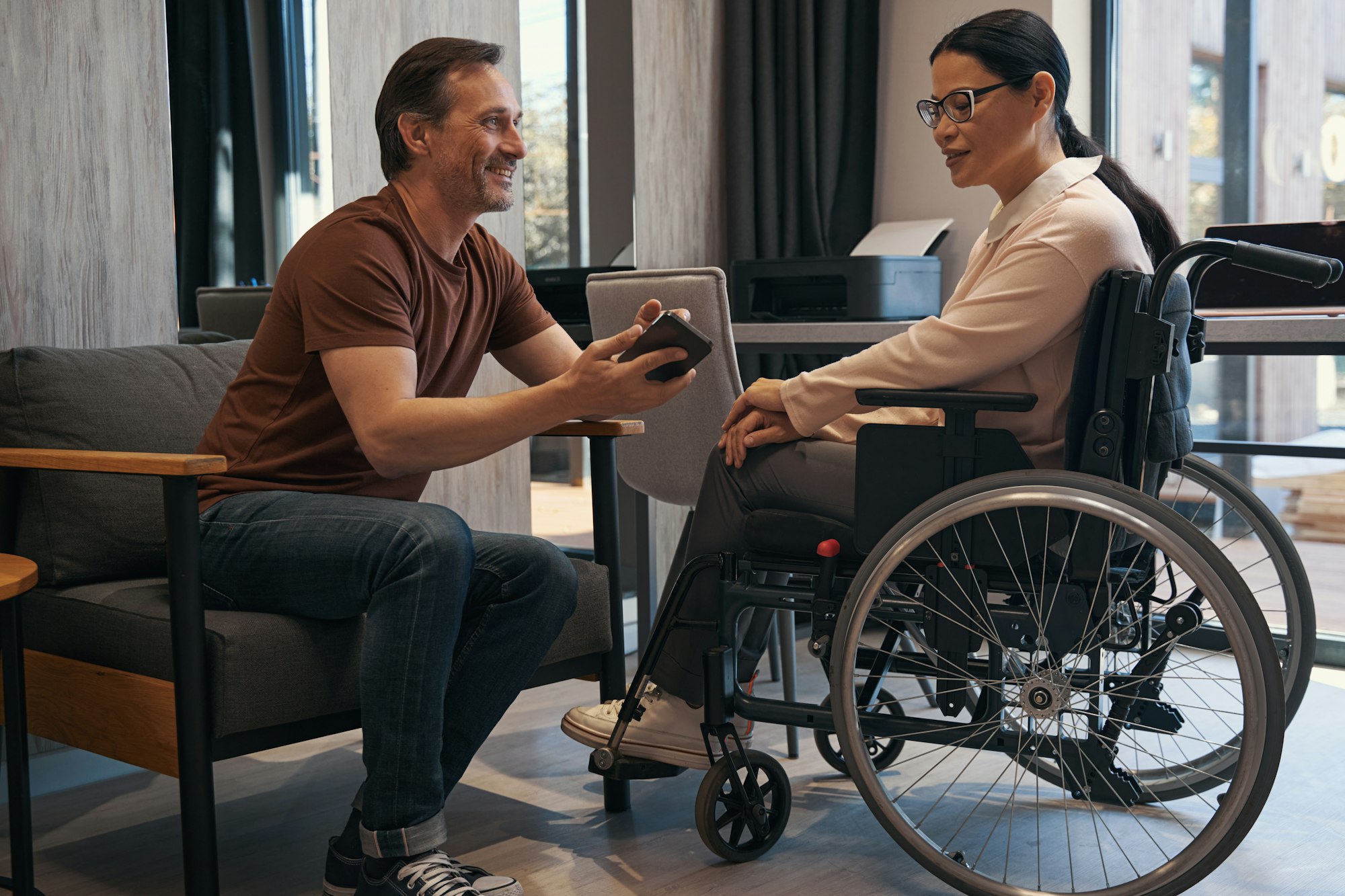 Jolly man with smartphone in office with female with disability